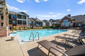 A pool surrounded by lounge chairs and buildings in the background. at Somerset Oaks Apartment Homes, Olathe